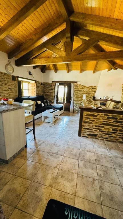 Cocina rústica con techo de vigas de madera, paredes de piedra, suelo de baldosas y armarios blancos.