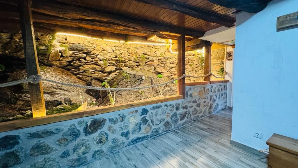 Patio cubierto con muro de piedra, vigas de madera en el techo y paredes azules con vistas a una ladera rocosa.