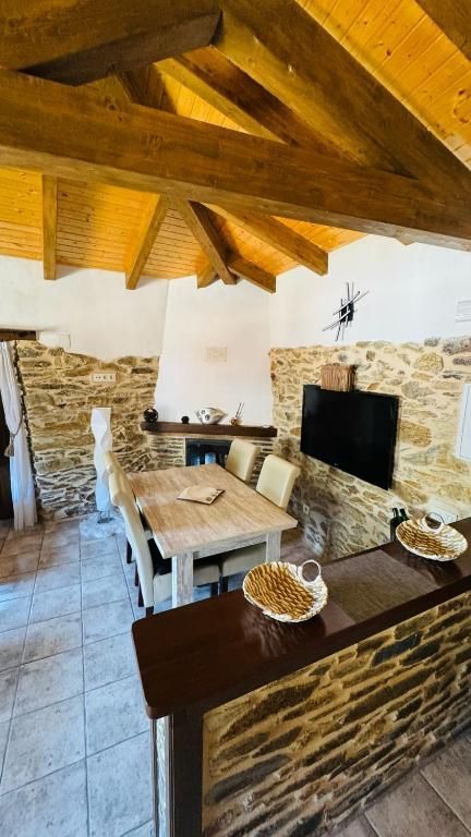 Acogedora sala con chimenea de piedra, vigas de madera a la vista, mesa de comedor y televisor montado sobre el hogar.