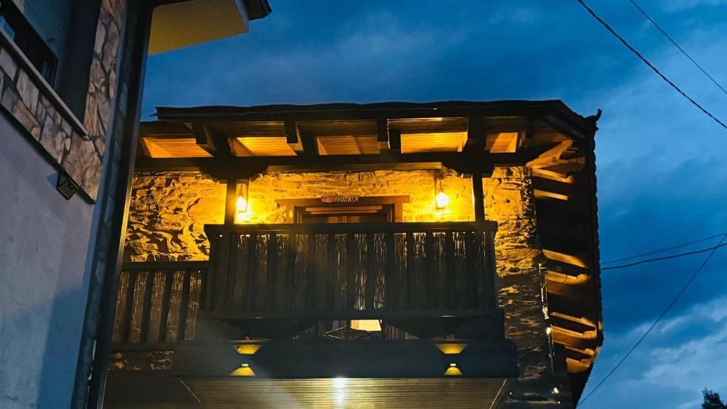 Balcón rústico de piedra cálidamente iluminado por la noche, con barandillas de madera y faroles brillantes.