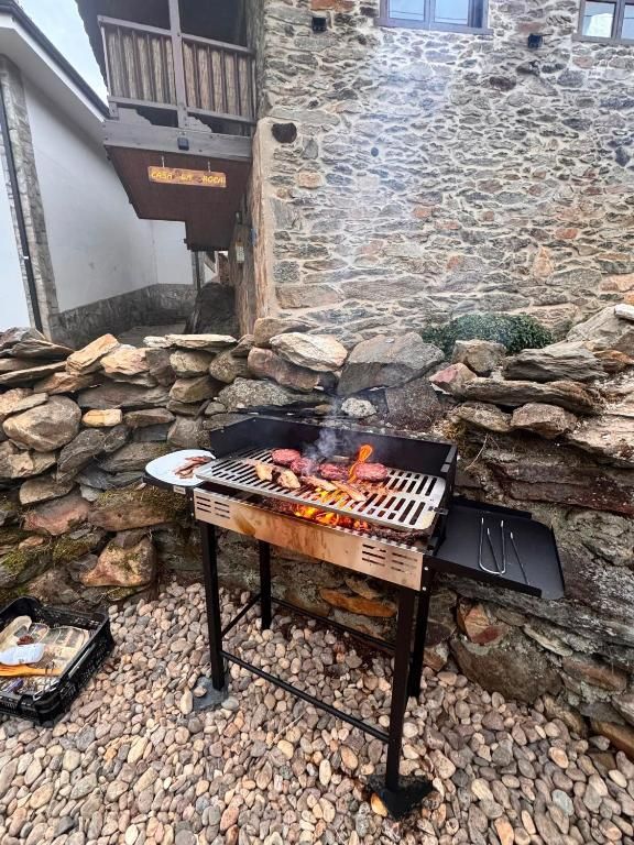 Parrilla con comida y llamas junto a un muro de piedra y un patio de grava al aire libre.