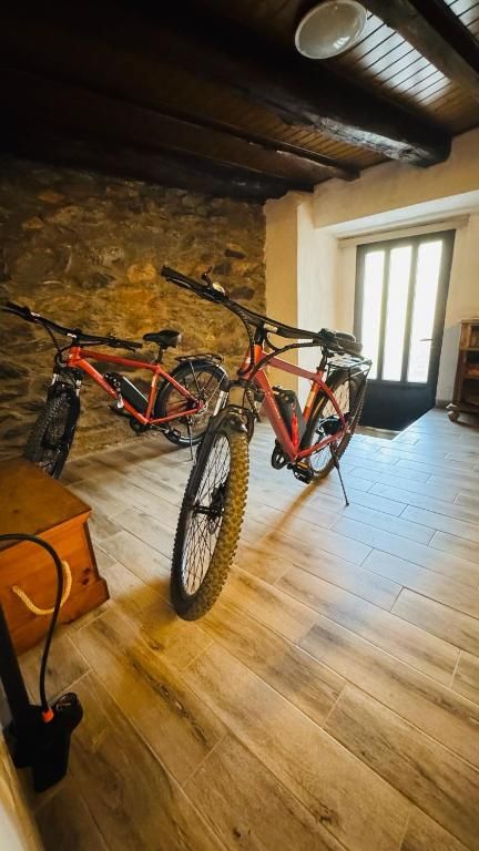 Dos bicicletas de montaña en una habitación rústica con paredes de piedra, vigas de madera y una puerta luminosa.