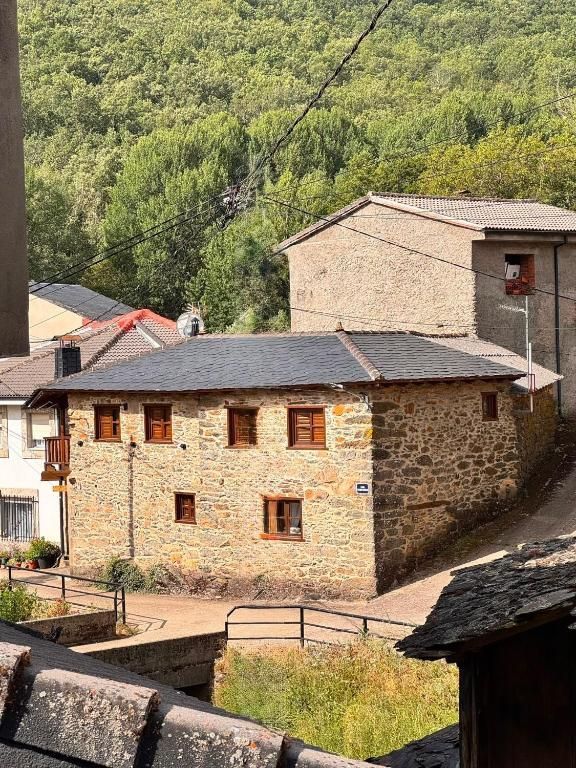 Casas de piedra con contraventanas rojas en la ladera de una colina, con un denso bosque verde al fondo.