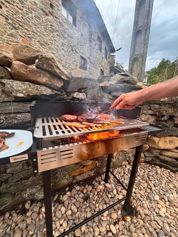 Asar comida a la parrilla sobre fuego abierto en una barbacoa de metal al aire libre junto a un muro de piedra.