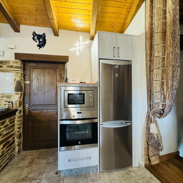 Rincón de cocina rústico con nevera de acero inoxidable, horno empotrado, vigas de madera y puerta de madera.