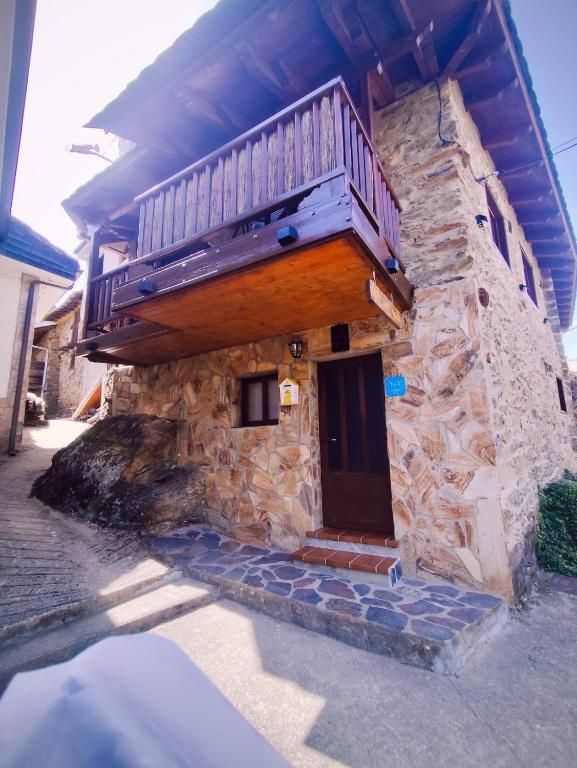 Casa de piedra con balcón de madera y puerta de entrada en una calle estrecha y soleada.