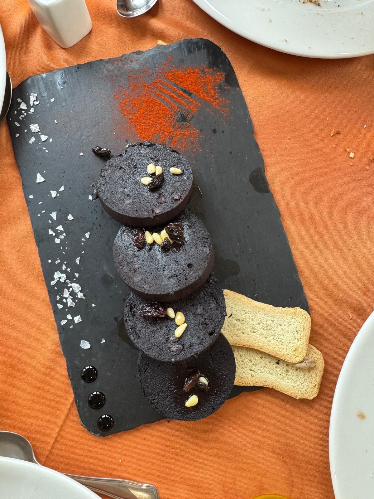 Porciones de postre de chocolate sobre una pizarra negra, adornadas con frutos secos, sobre un mantel naranja.