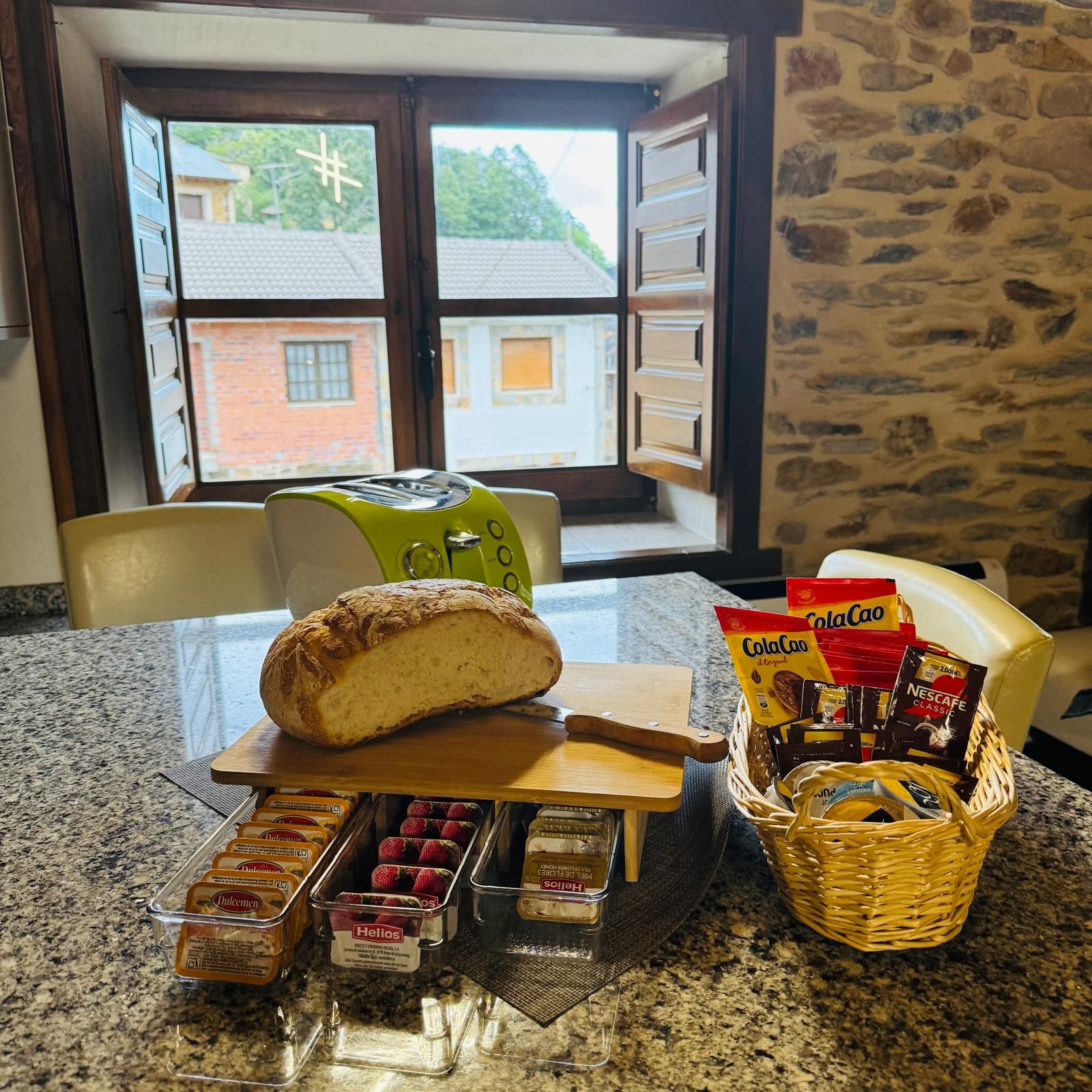 Encimera de cocina con pan rebanado, pasteles, dulces y una cesta junto a una ventana abierta.