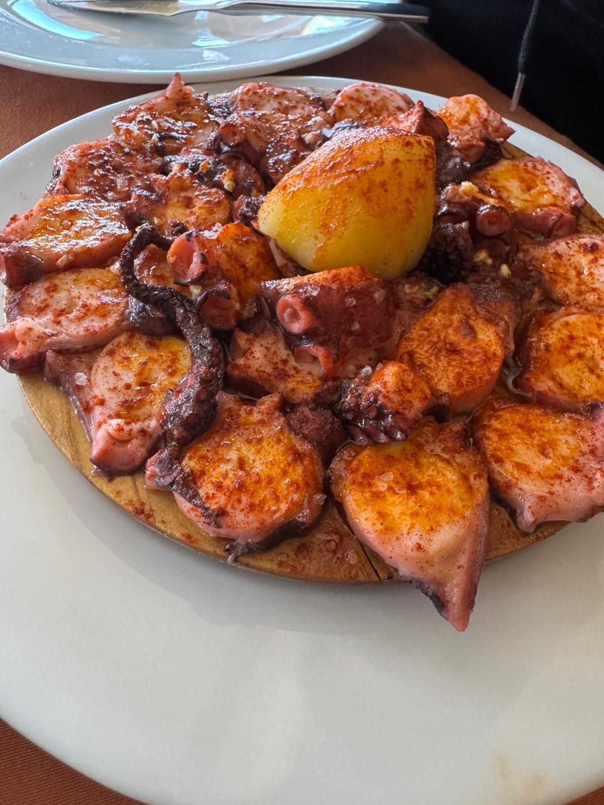 Pulpo a la parrilla con rodaja de limón en un plato blanco.