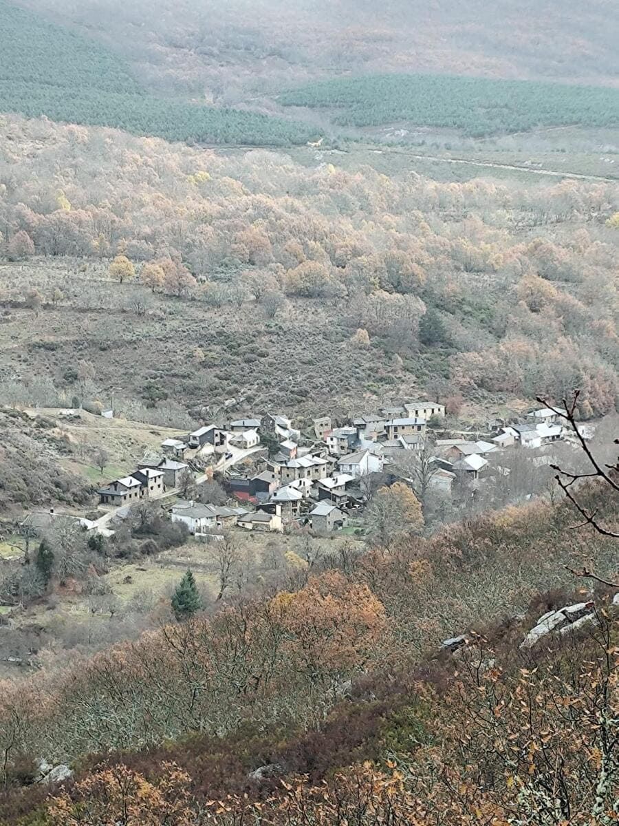 Pequeño pueblo en un valle brumoso de otoño, rodeado de colinas boscosas con follaje en tonos naranjas y verdes apagados.