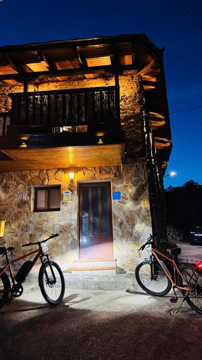 Casa de piedra cálidamente iluminada por la noche, con dos bicicletas aparcadas fuera y un balcón sobre la puerta.