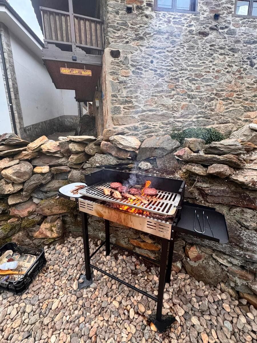 Pequeña parrilla de carbón con comida y llamas en un patio de piedra junto a un edificio rústico.