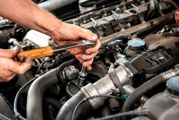 Un hombre está trabajando en el motor de un automóvil con una llave inglesa.