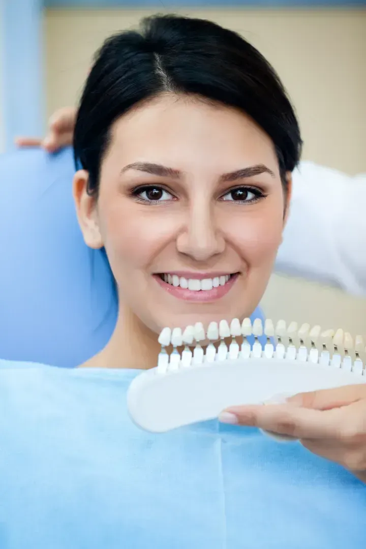 Una mujer está sentada en una silla dental sosteniendo una tabla de colores de dientes.