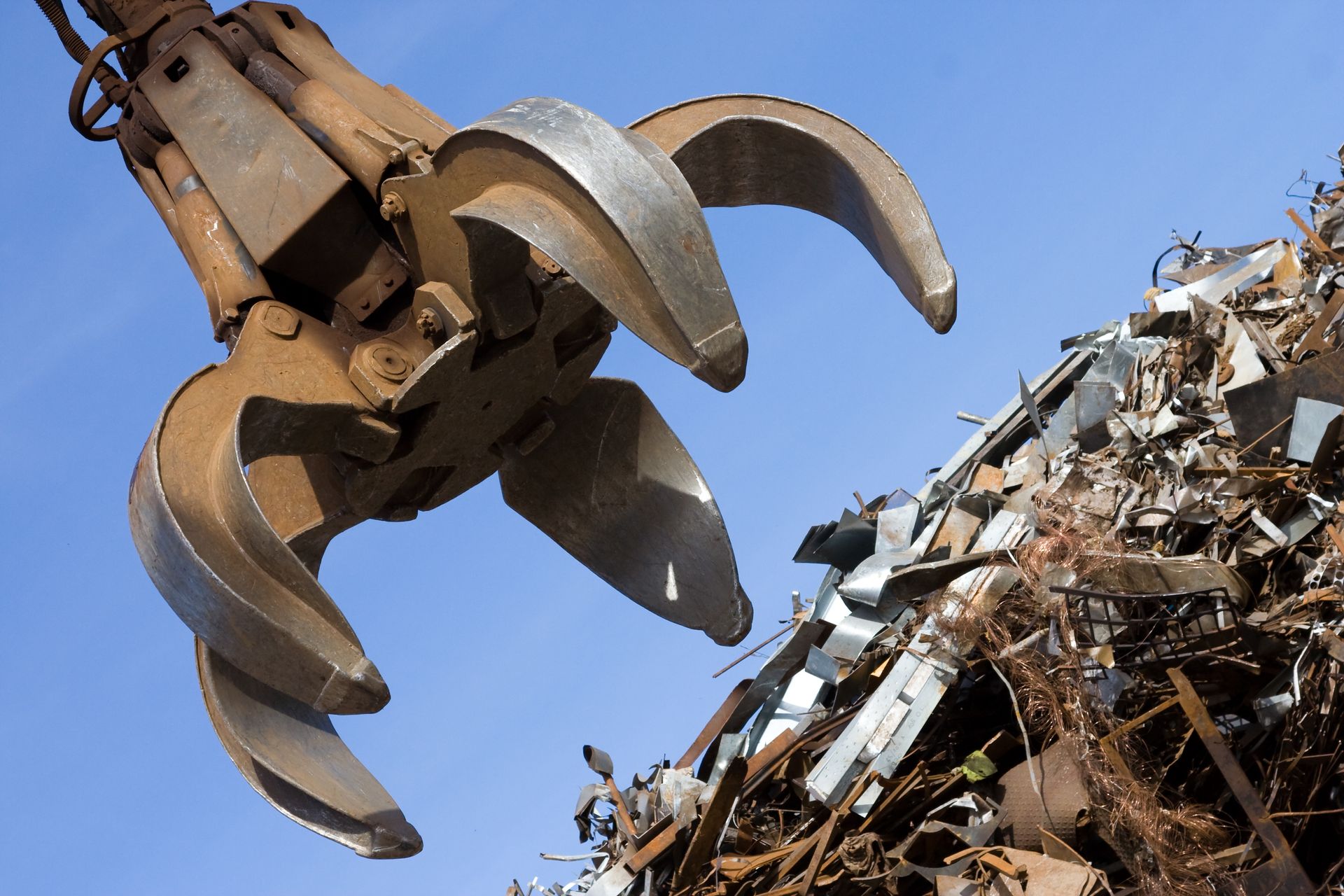 Une pelle mécanique ramasse des morceaux de métal dans une casse sous un ciel bleu.