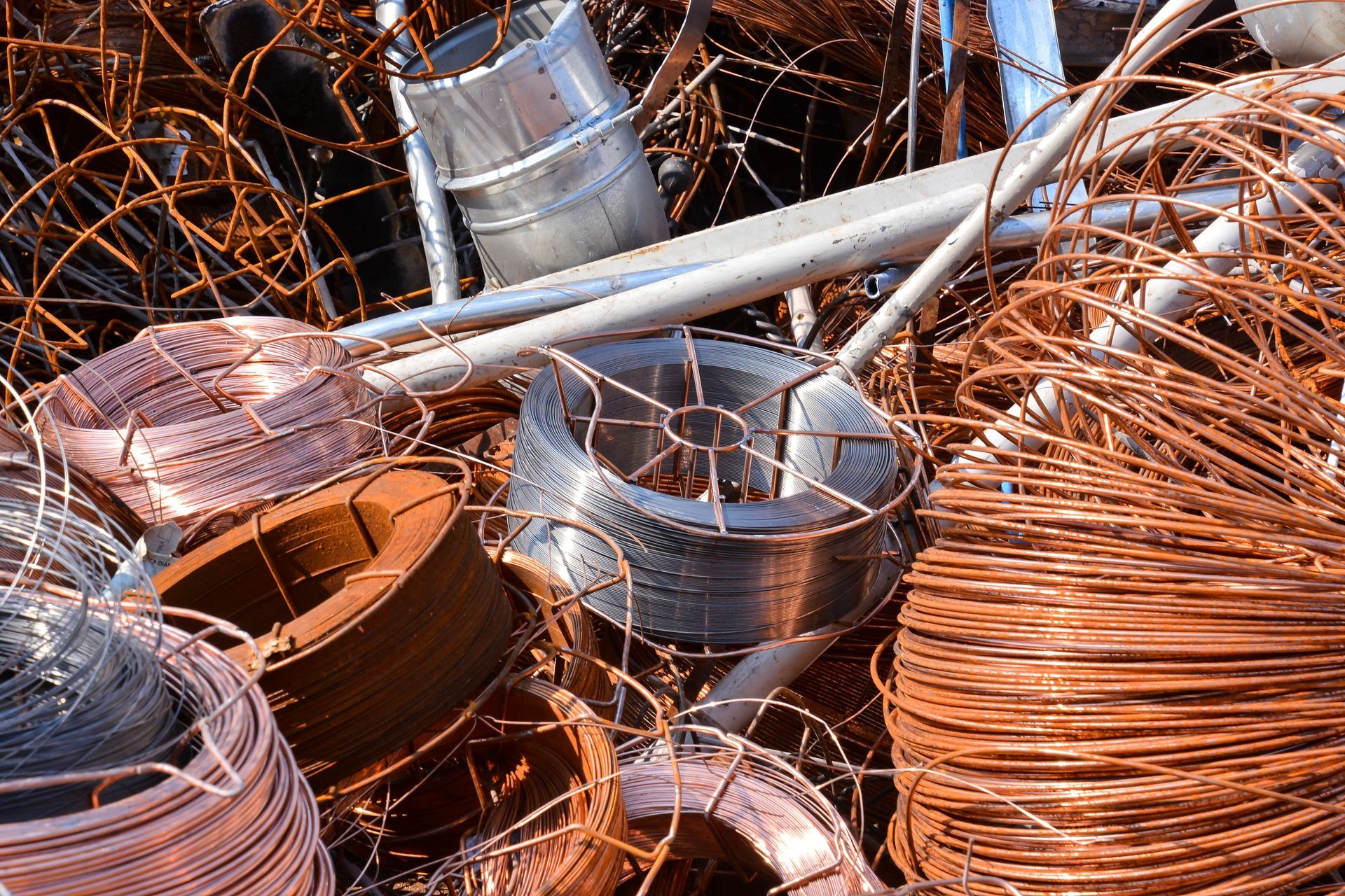 Des bobines de fil de cuivre et des déchets métalliques entassés dans une casse ou un centre de recyclage.