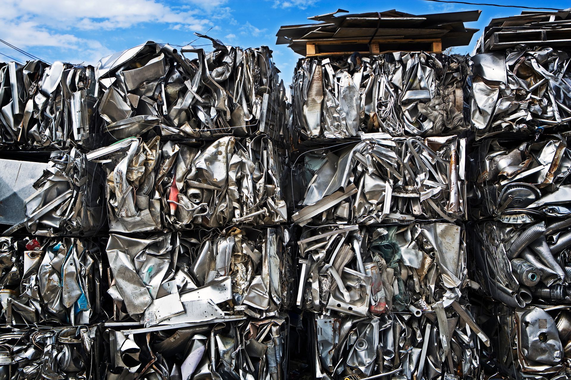 Des ballots de ferraille broyée empilés dans un centre de recyclage sous un ciel bleu.