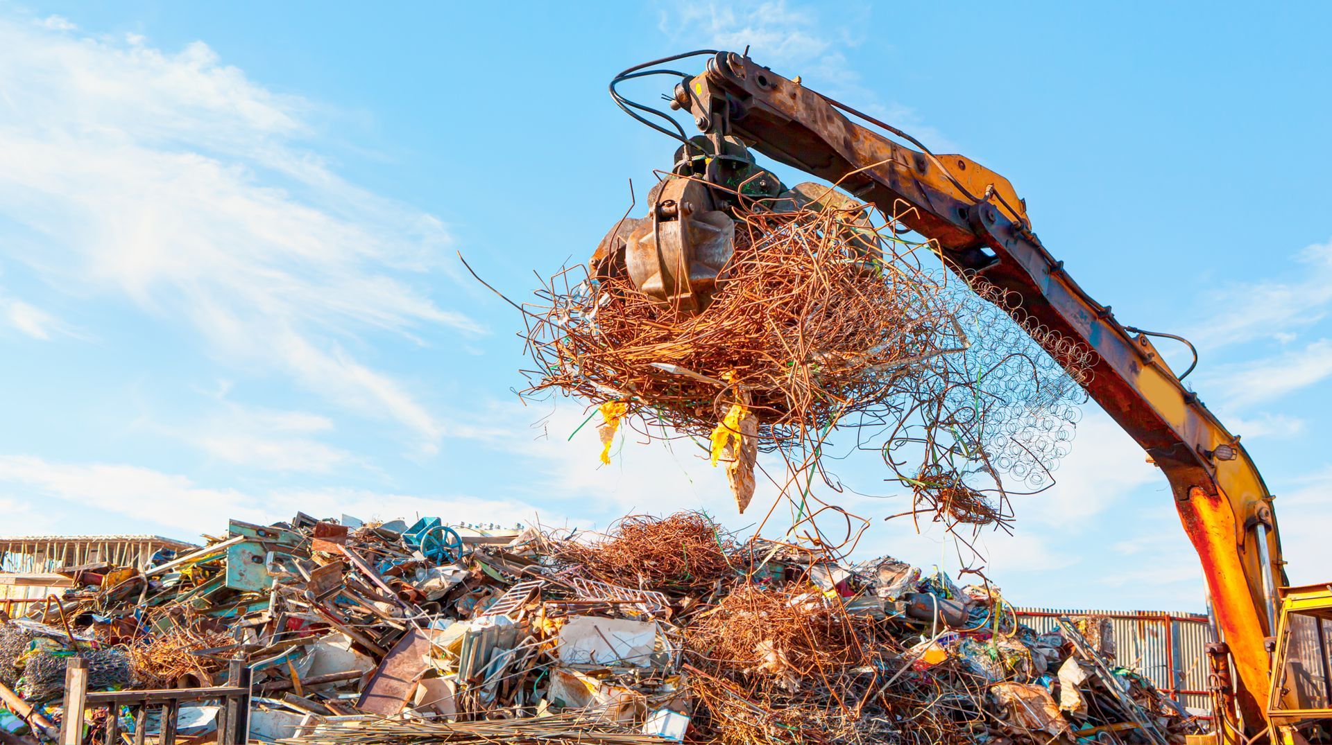 Une excavatrice charge de la ferraille dans un camion sur un site de recyclage sous un ciel bleu