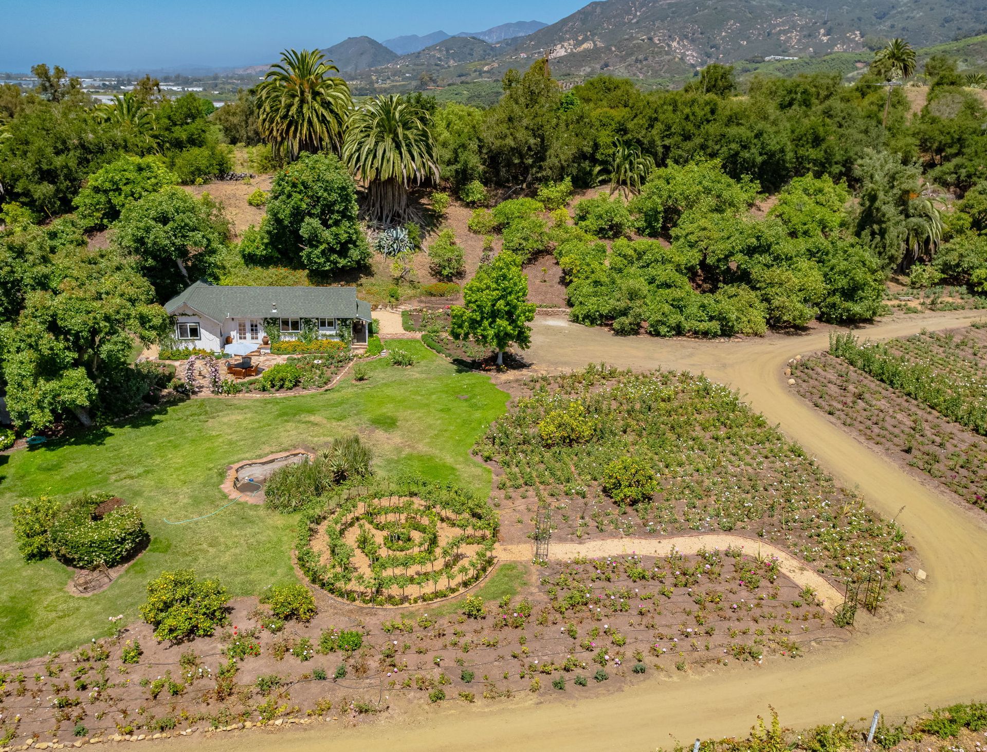 Aerial view of a landscaped garden with circular flower beds, a small house, and mountains in the background