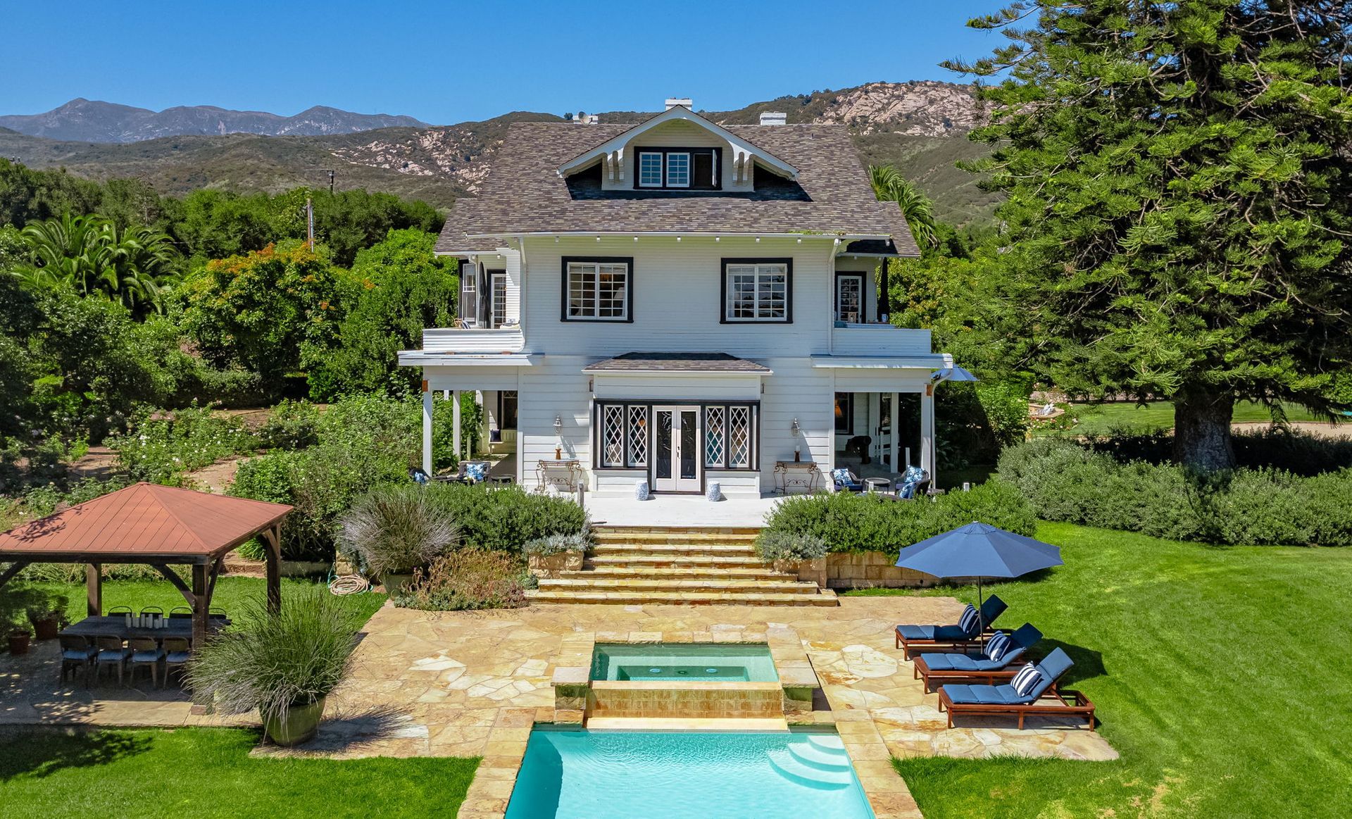 White house with pool, patio loungers, and mountain views in a sunny garden