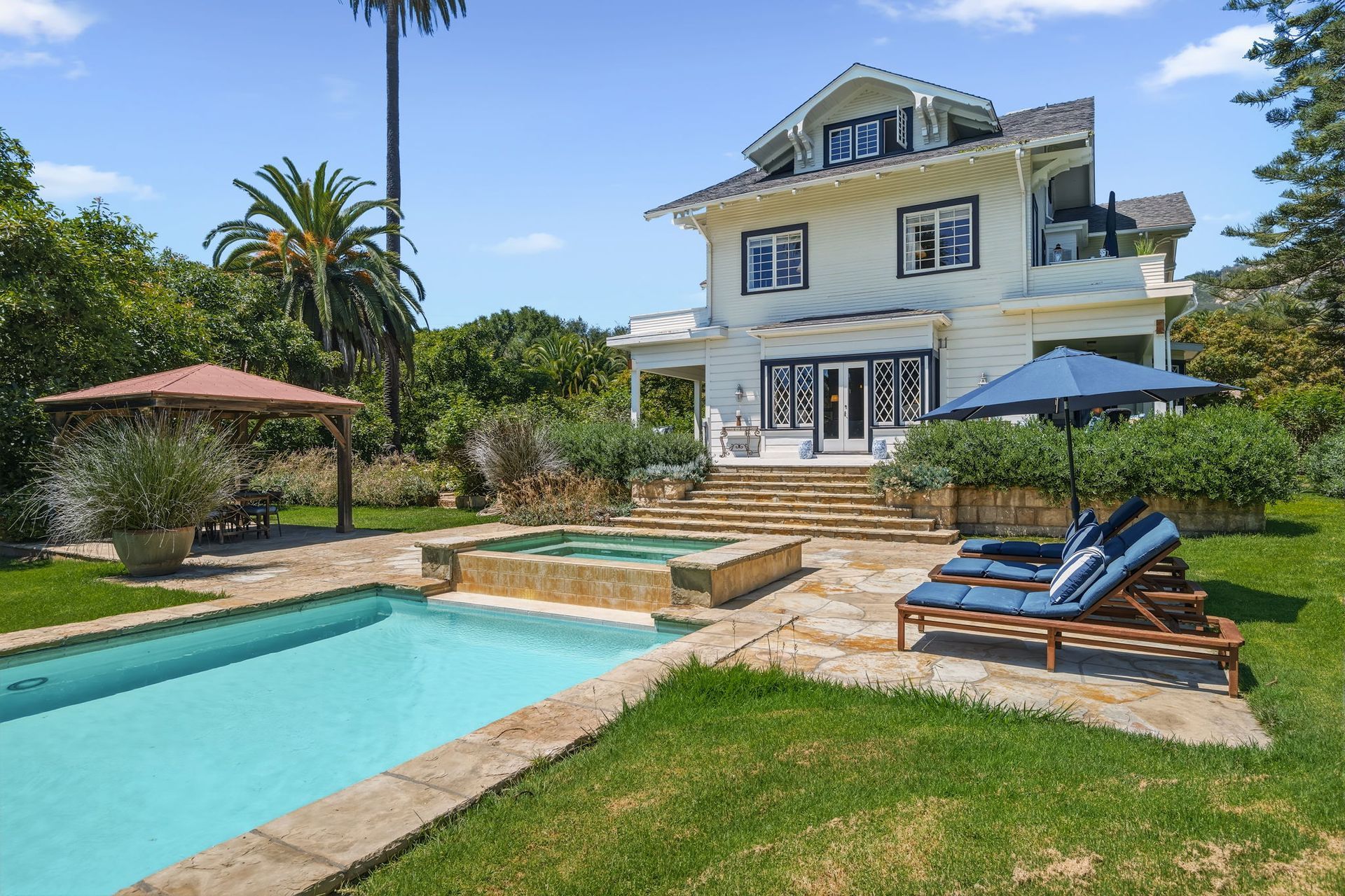 Sunny backyard with turquoise pool, lounge chairs, umbrellas, and a cream-colored house