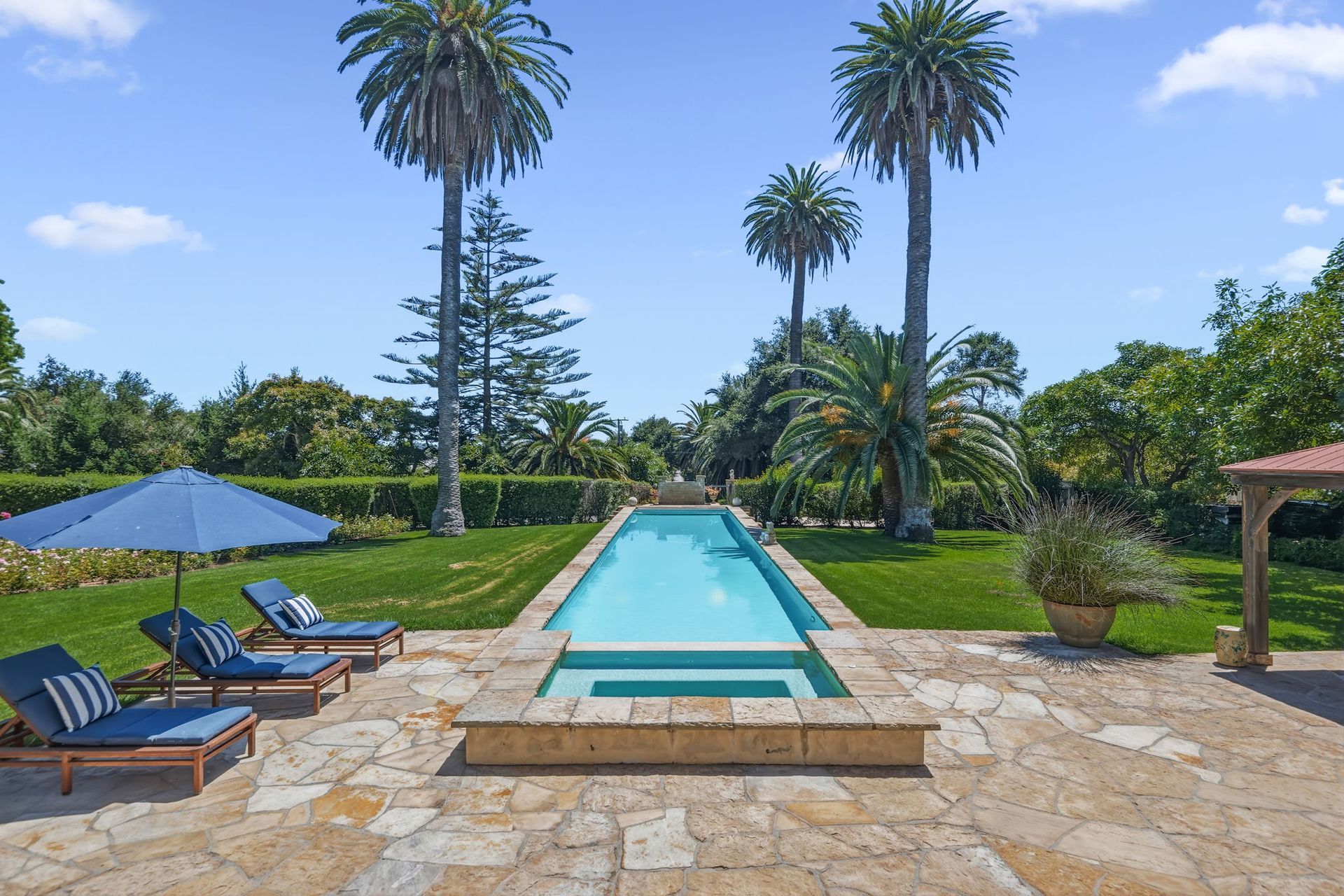 Resort pool with lounge chairs, umbrellas, and palm trees under a bright blue sky