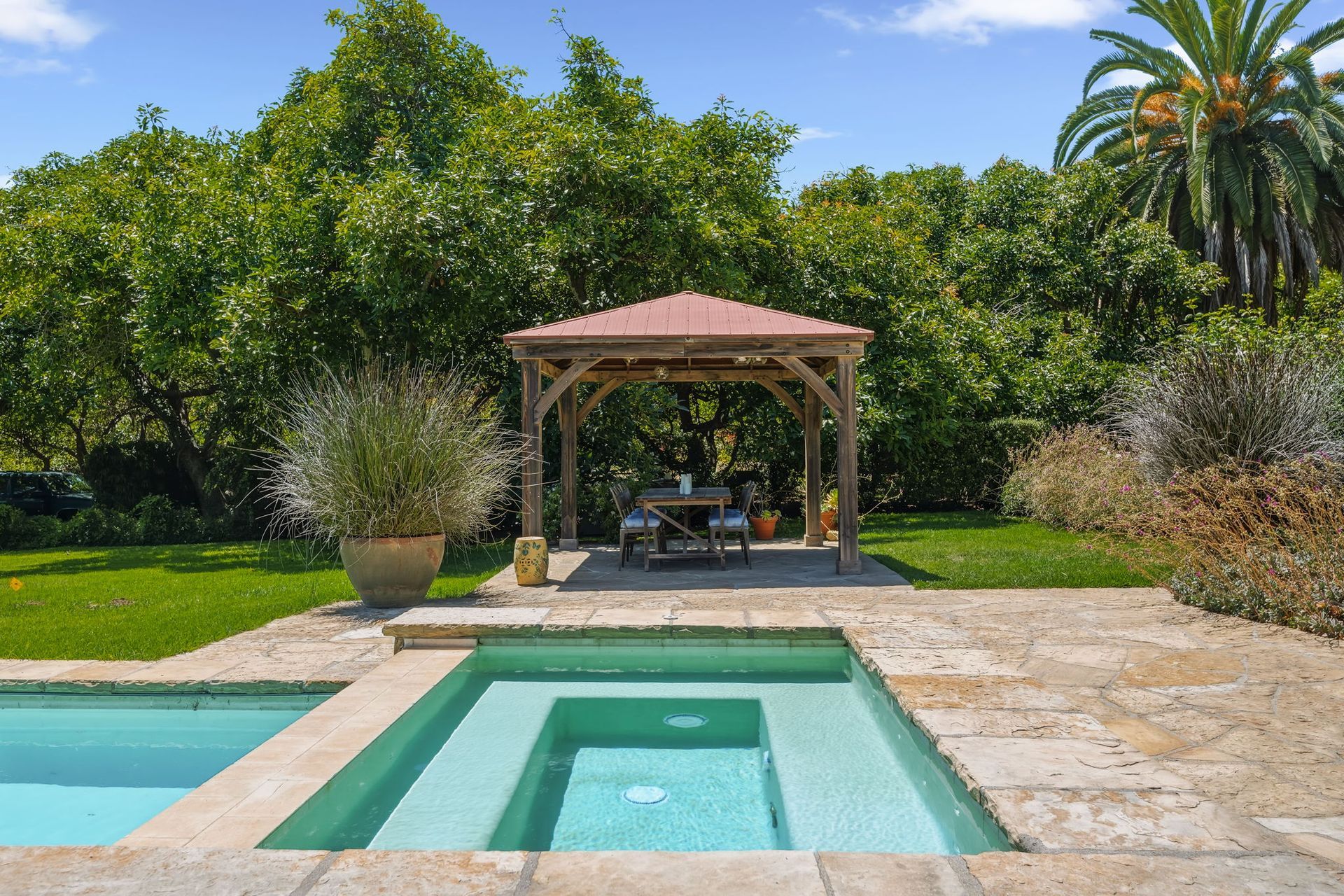 Backyard pool with hot tub, gazebo, and lush tropical landscaping under a blue sky