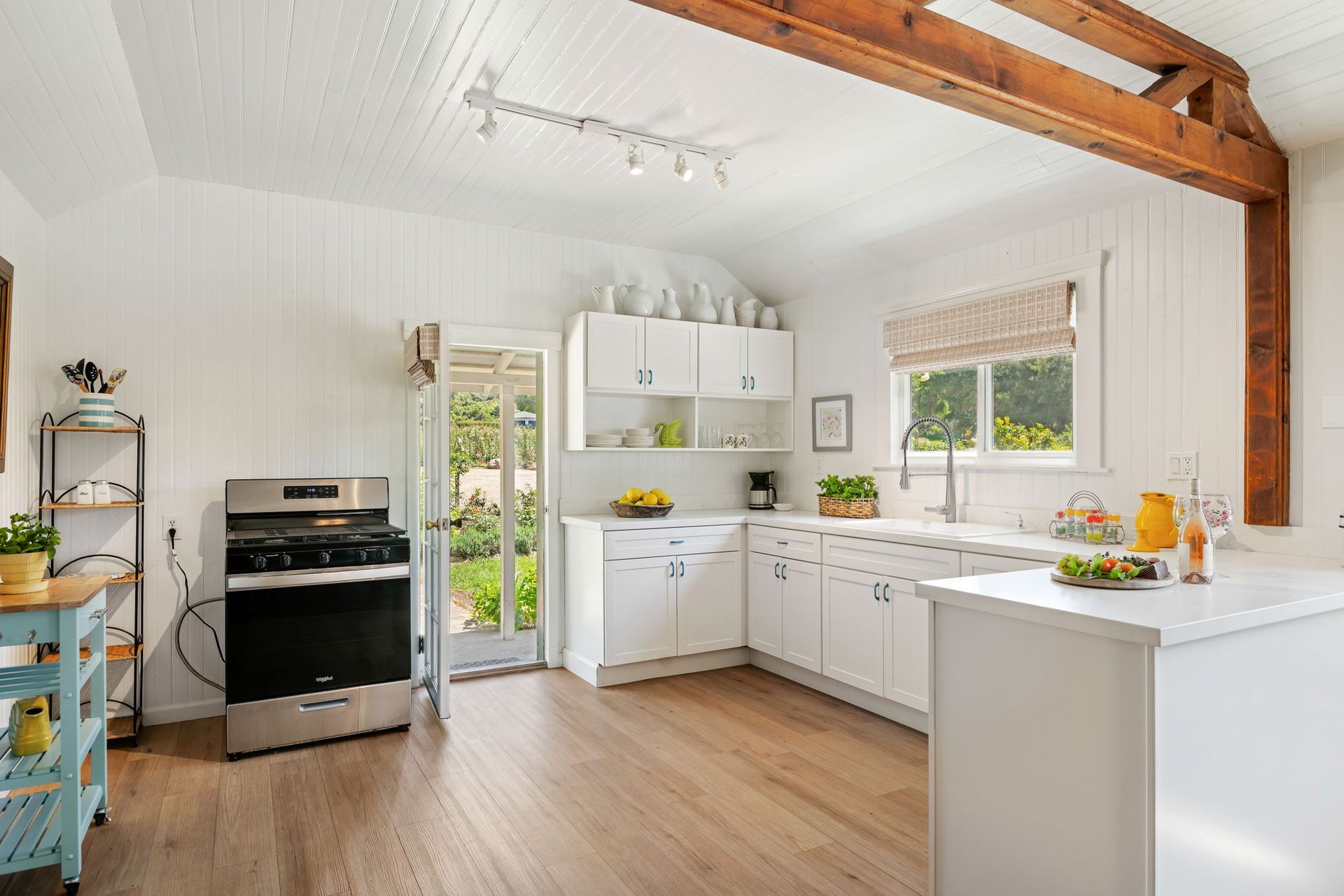 Bright white kitchen with wood beams, stainless stove, and windows overlooking greenery