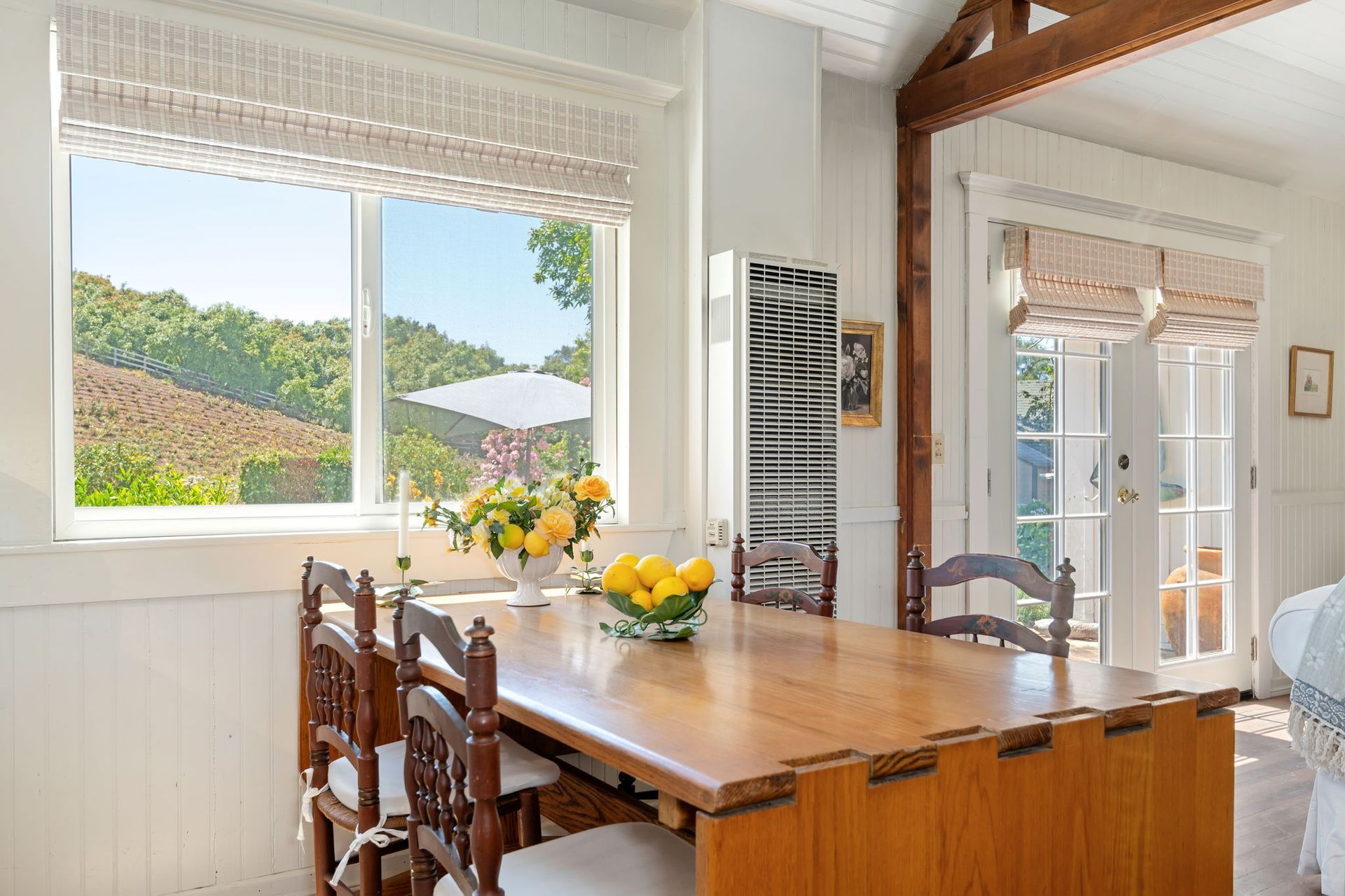 Bright dining room with wooden table, flowers, and large window overlooking greenery