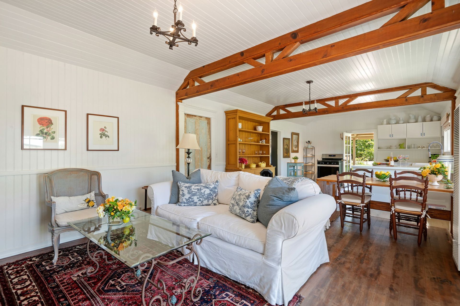 Bright living room with white sofa, wooden beams, red rug, and open kitchen dining area
