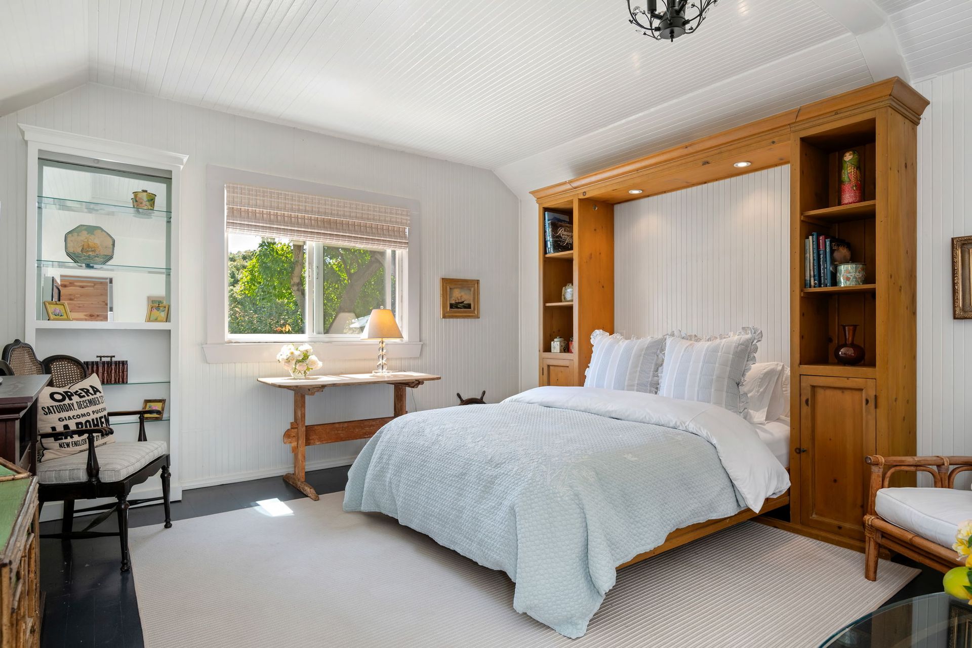 Bright bedroom with a white bed, wooden headboard, desk by window, and a chair near the door.