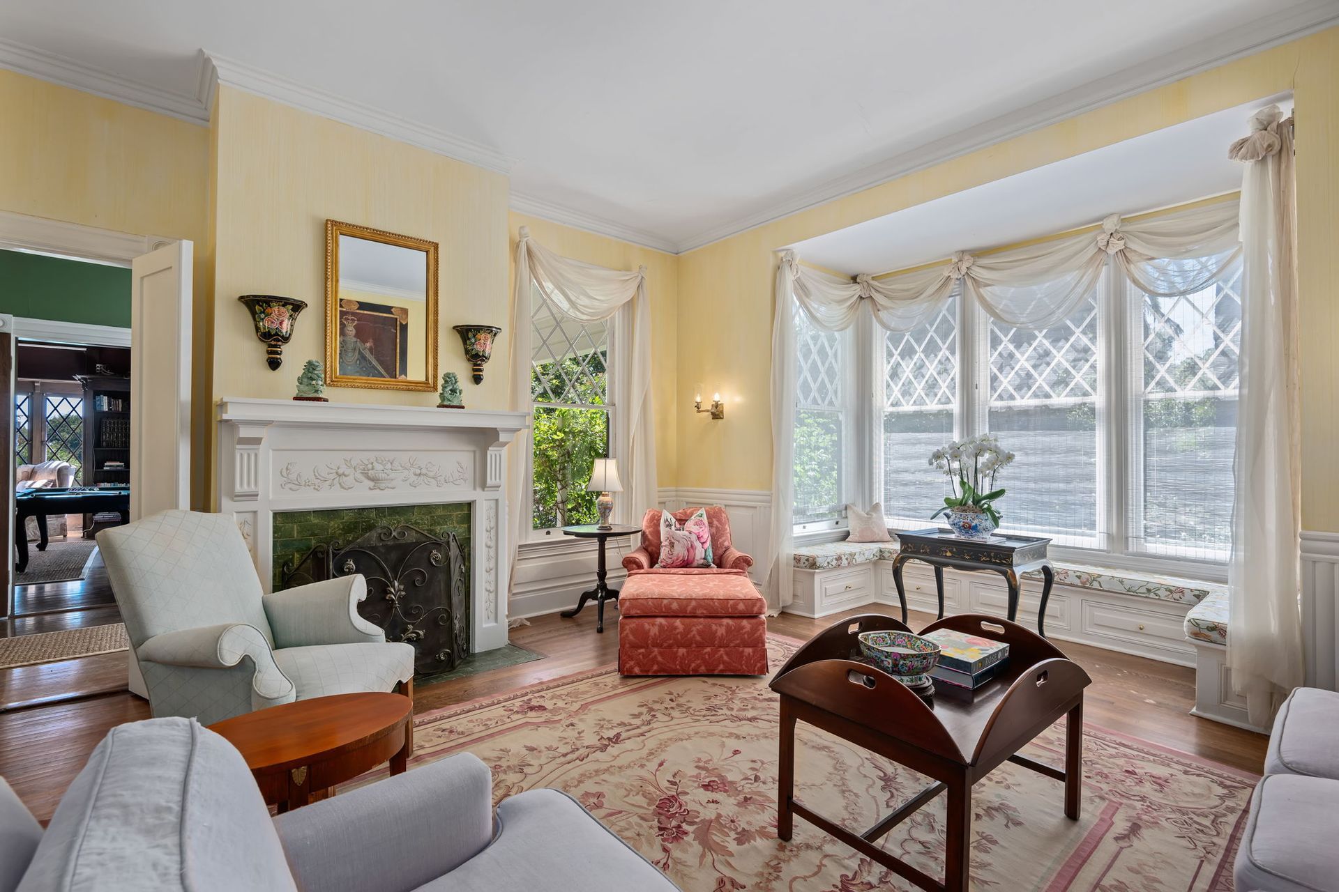 Elegant living room with fireplace, pale yellow walls, white chairs, and large bay window with curtains