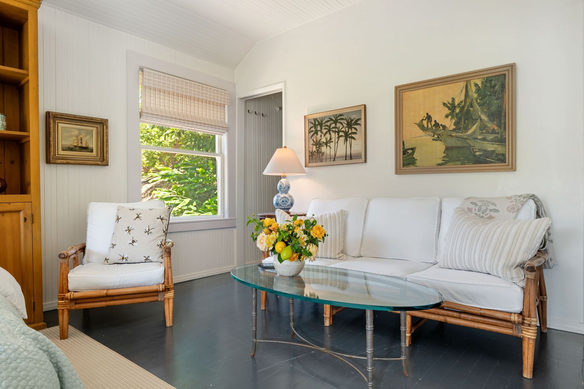 Bright sunroom with wicker chairs, glass table, flowers, and framed art near a window