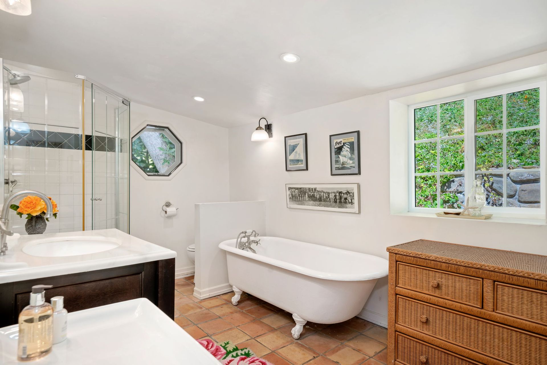 Bright bathroom with freestanding tub, vanity, wicker cabinet, and window looking onto greenery