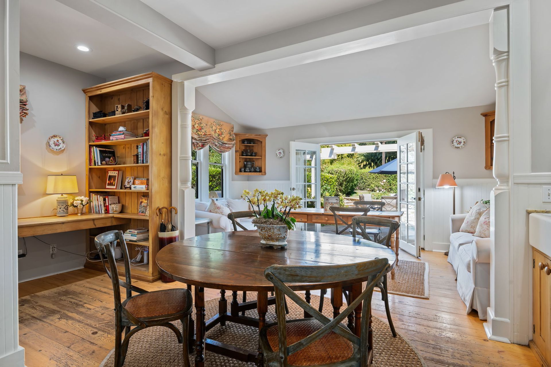 Bright dining room with wooden table, shelves, and open doors to a sunny garden