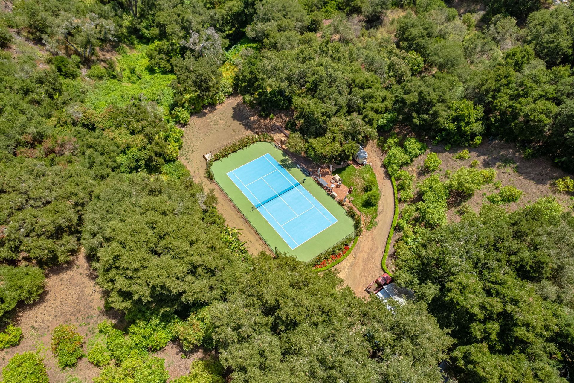 Aerial view of a turquoise rectangular pool surrounded by dense green trees and dirt paths