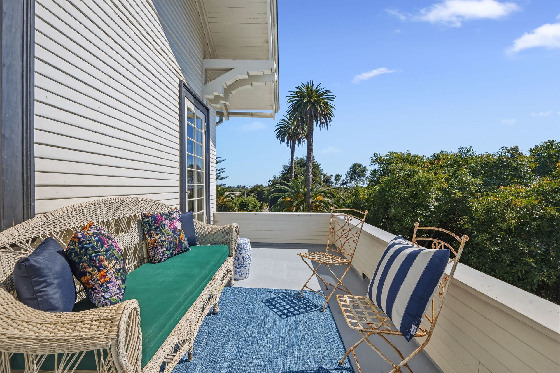 Cozy porch with wicker seating, green cushion, striped chair, blue rug, and ocean view beyond a white railing