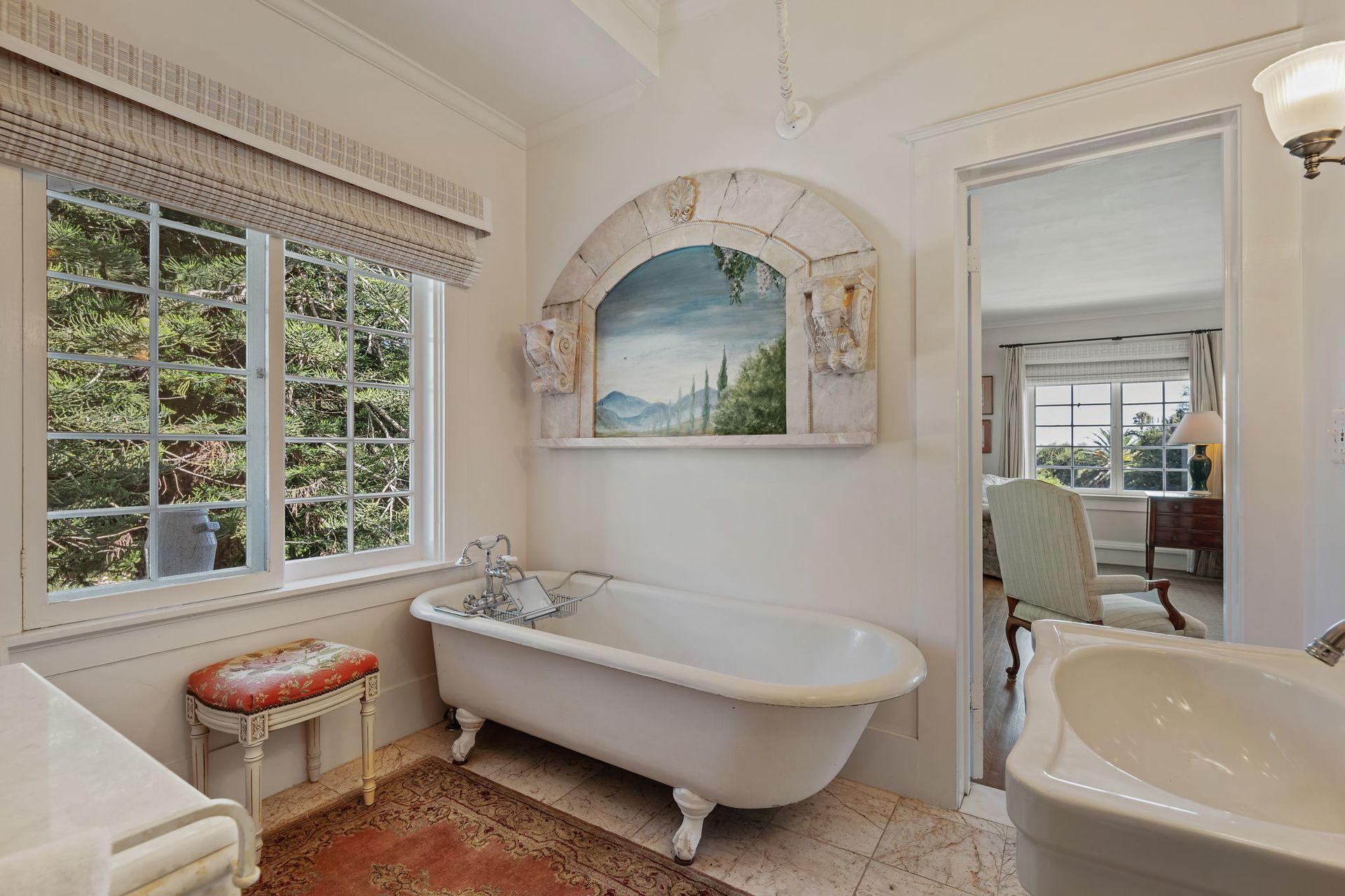 Bright bathroom with freestanding tub, tiled floor, double sinks, and a window overlooking greenery
