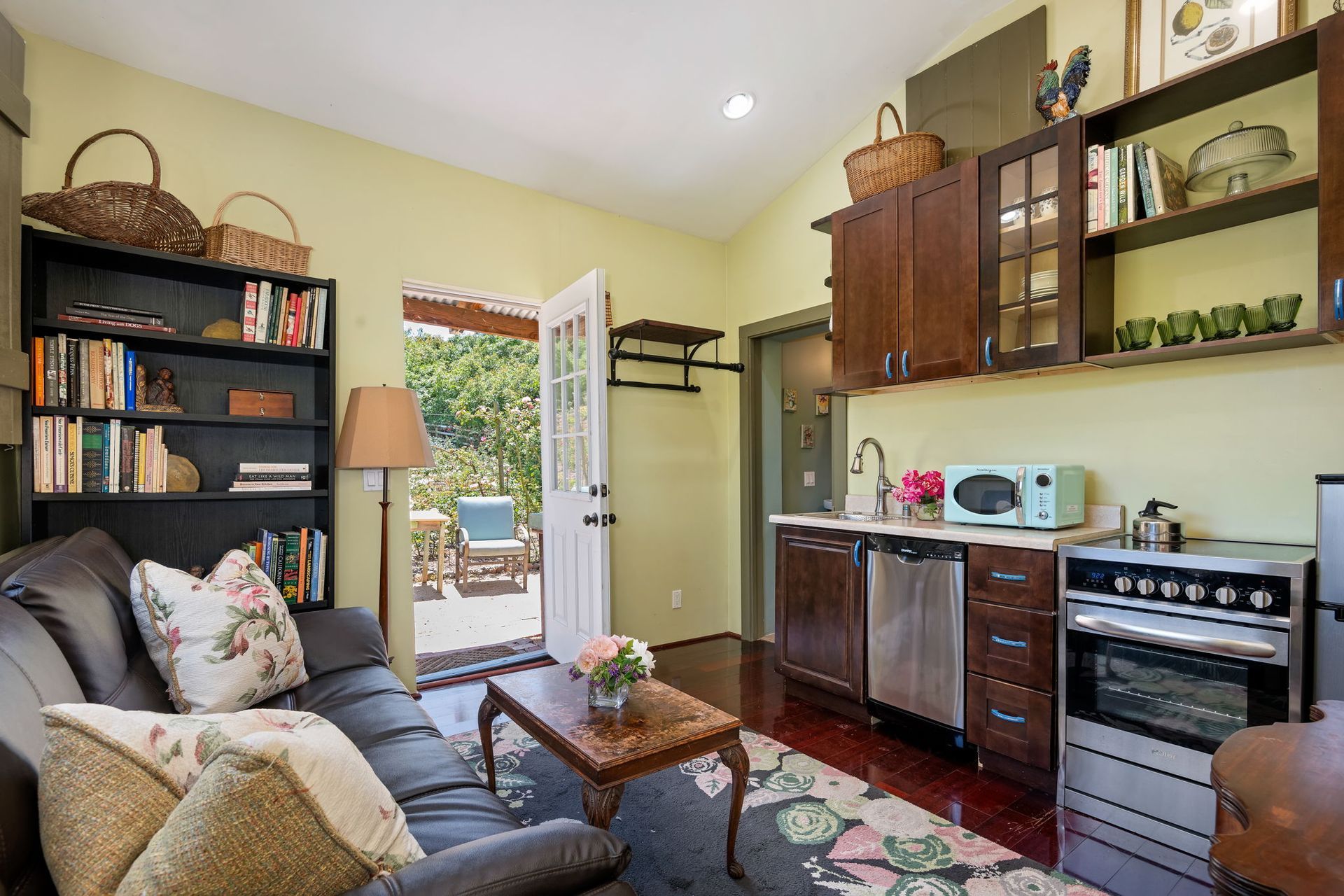 Cozy living room with sofa, bookshelf, coffee table, kitchen counter, and open door to a patio