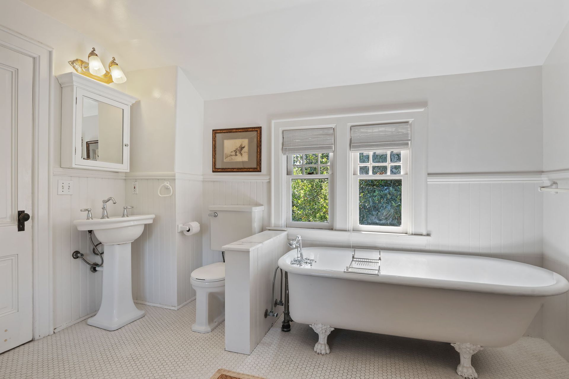 Bright white vintage bathroom with pedestal sink, clawfoot tub, toilet, and small window