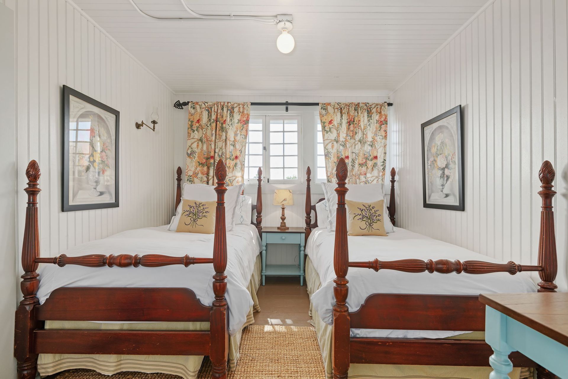 Bright twin bedroom with four-poster beds, floral curtains, and a window seat.