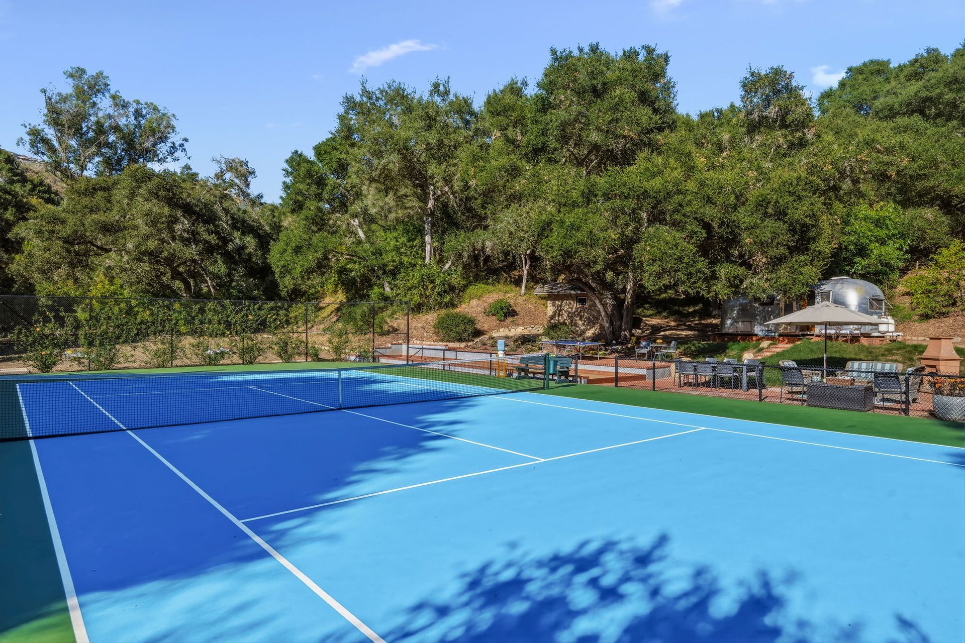 Outdoor tennis court with blue surface and trees in the background