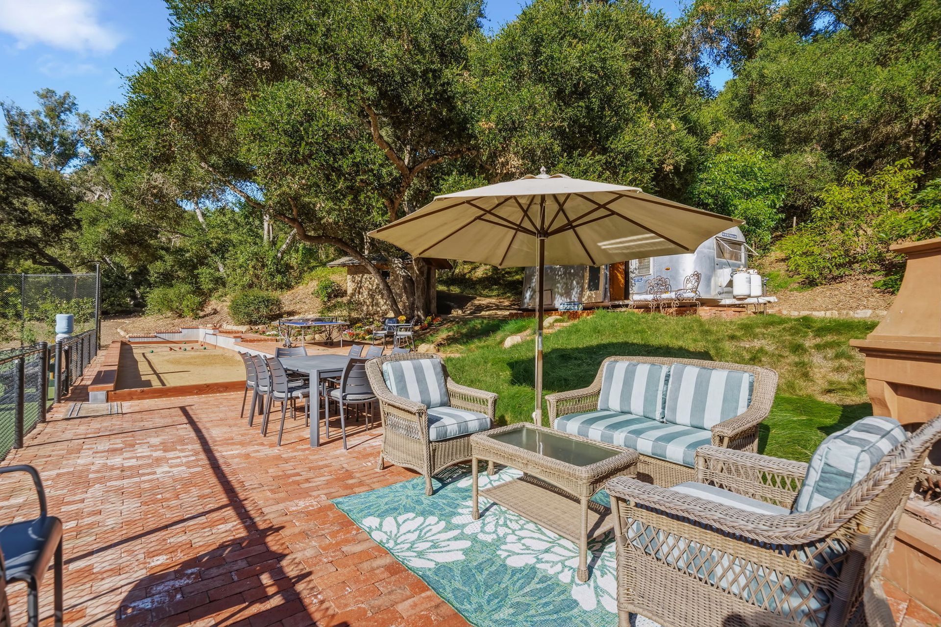 Outdoor patio seating with wicker chairs, striped cushions, umbrella, and brick paving amid trees