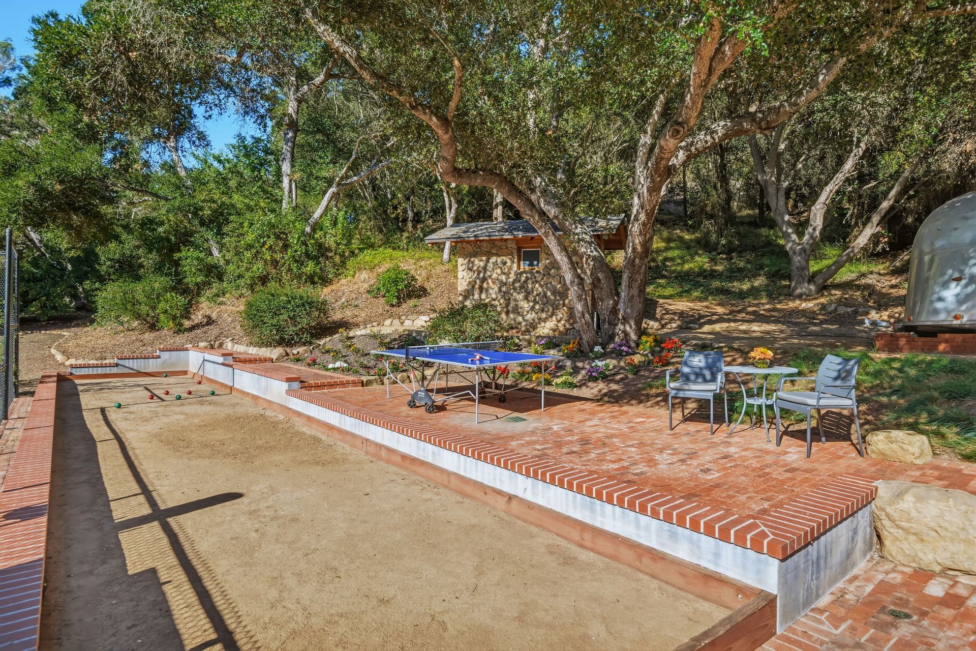 Brick patio with blue chairs and table beside a sandy area and trees in a backyard