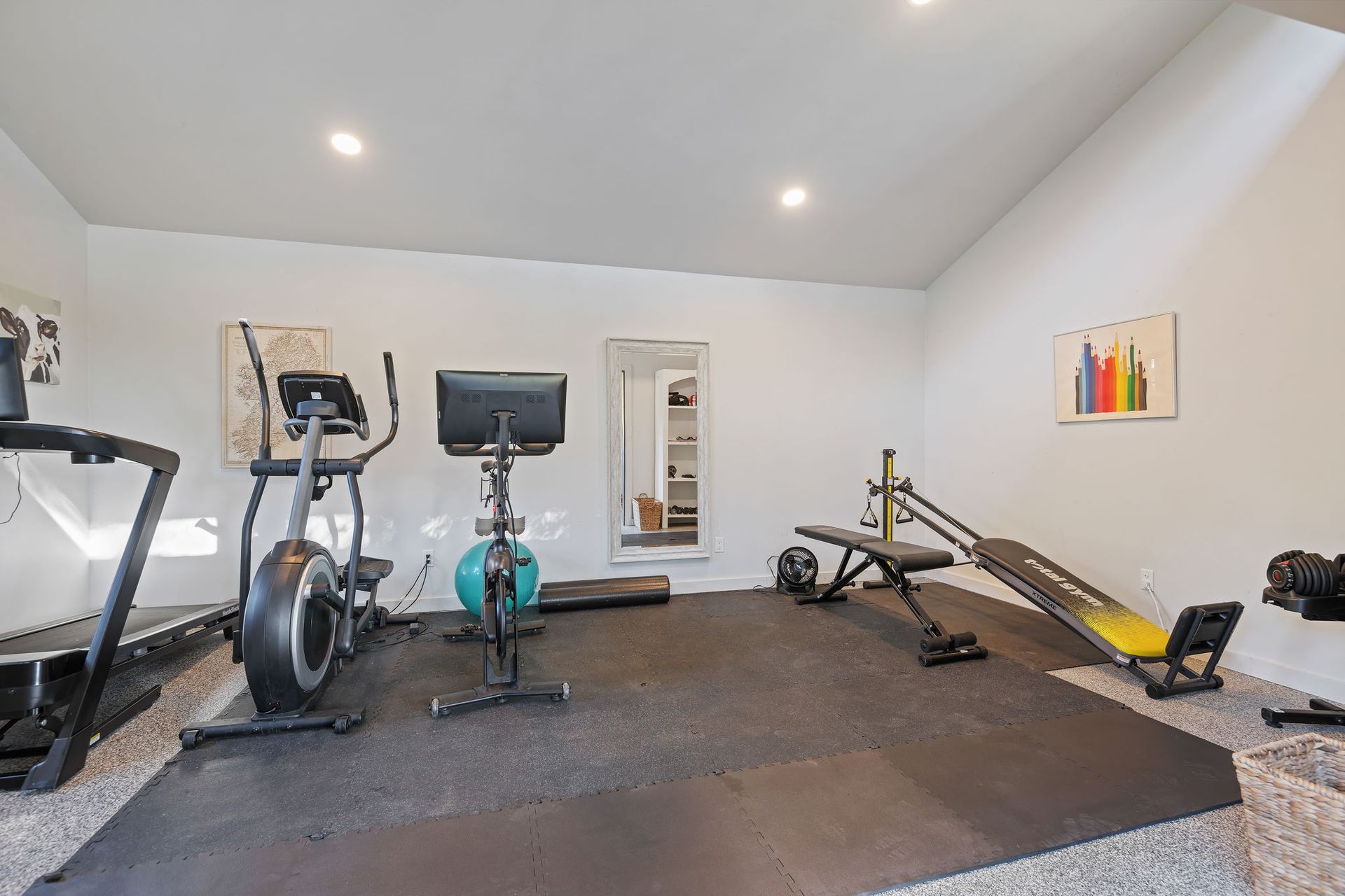 Home gym with treadmill, stationary bike, rowing machine, and weight bench on a carpeted floor.