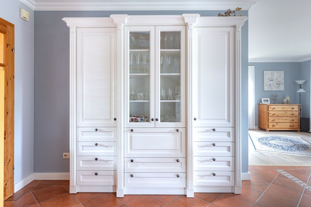 Ein großer weißer Schrank mit Glastüren und Schubladen in einem Wohnzimmer.