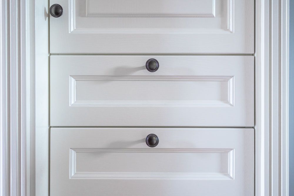 Eine Nahaufnahme eines weißen Schranks mit drei Schubladen und schwarzen Knöpfen.