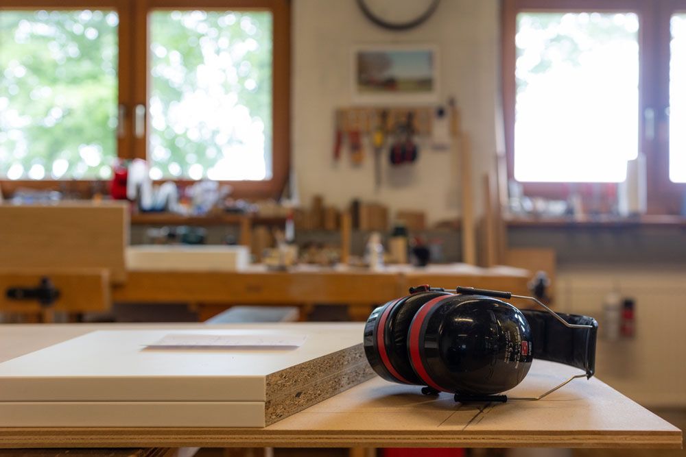 Ein Paar Ohrenschützer liegt auf einem Holztisch in einer Werkstatt.