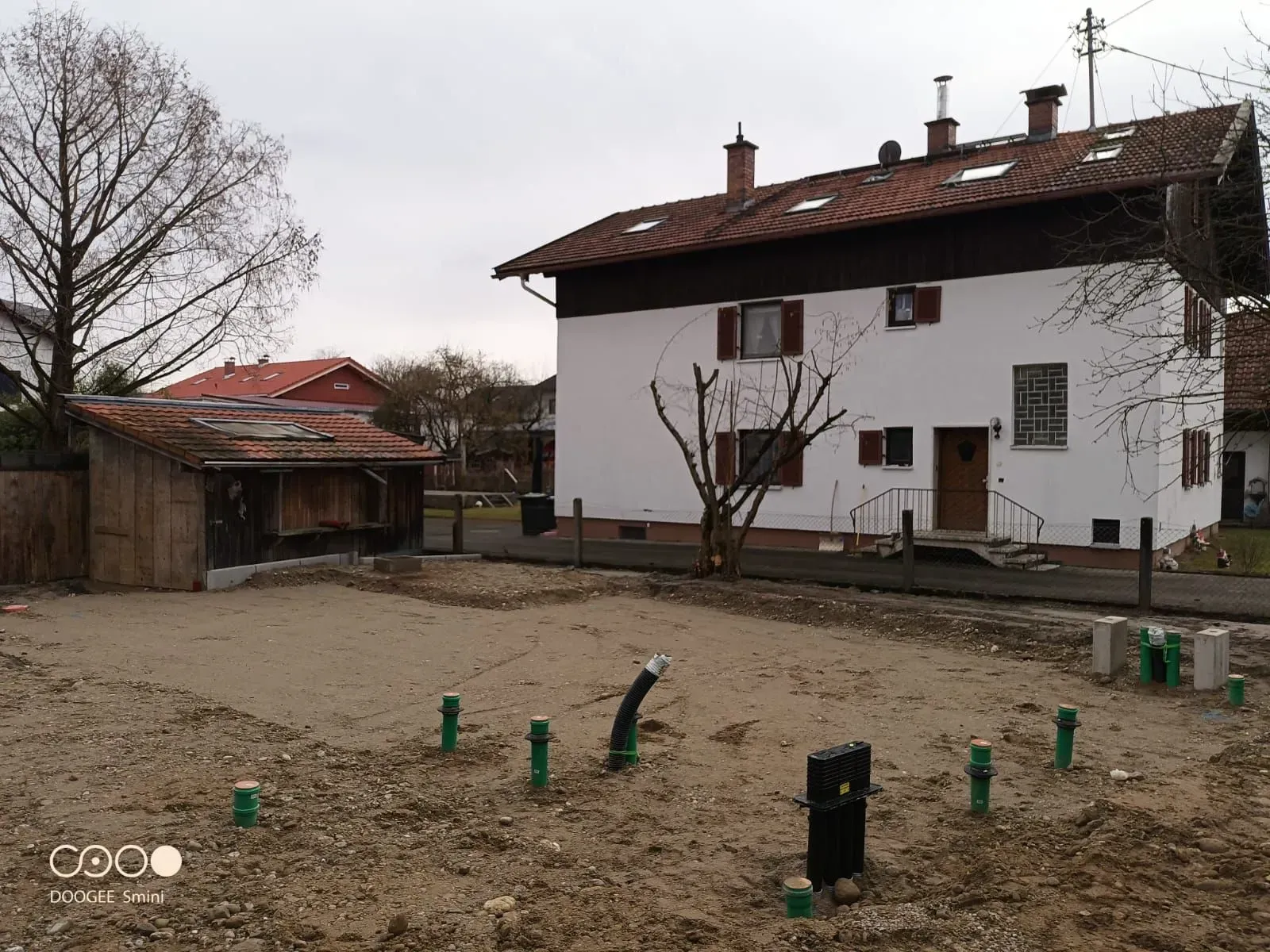 Ländlicher Hof mit einem weißen Haus, einem Schuppen mit rotem Dach und kahlem Boden unter einem bedeckten Himmel