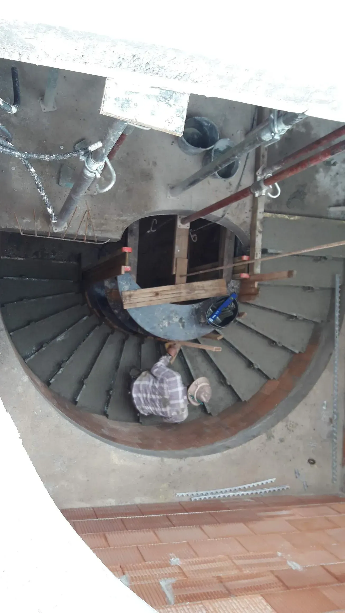 Draufsicht auf eine Wendeltreppe im Inneren eines Gebäudes, mit einer Person in der Nähe des unteren Endes.
